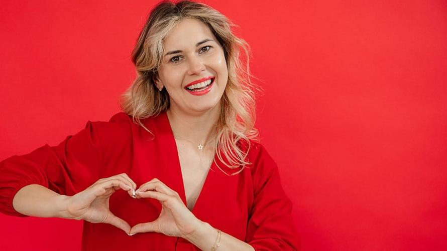woman in front of red background with heart hands